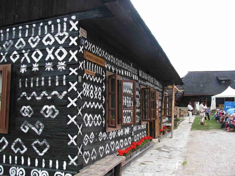 Bližší pohľad na ornamentálnu výzdobu geometrickými vzormi vonkajších stien nízkeho zrubového obytného domu.