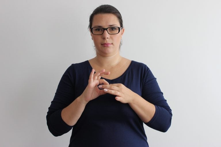 Žena predvádza posunok pre nepočujúcich, prstami obidvoch rúk naznačuje spojené oká reťaze.