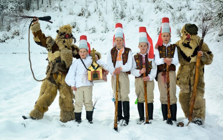 A group of masked nativity scenes in a snowy landscape, a winter forest in the background.