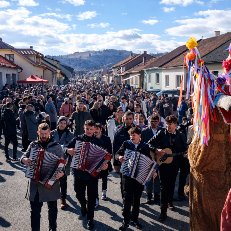 Ulica medzi domami plná ľudí. V pozadí kopec.