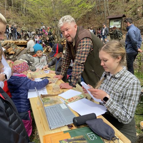 Ľudia pri stole s papiermi, knihami a počítačom uprostred lesa.