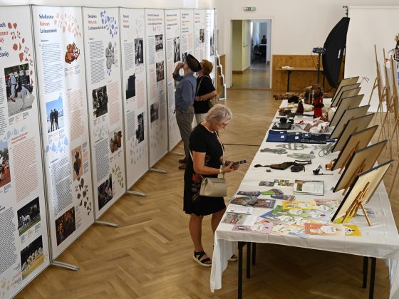 Tri osoby prezerajúce si osvedčenia o zápise a trojrozmerné ukážky k prvkom zapísaných v Reprezentatívnom zozname NKD ľudstva UNESCO. Za nimi banery k rovnakej téme.