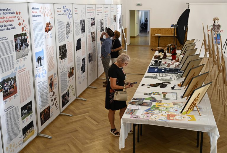 Tri osoby prezerajúce si osvedčenia o zápise a trojrozmerné ukážky k prvkom zapísaných v Reprezentatívnom zozname NKD ľudstva UNESCO. Za nimi banery k rovnakej téme.